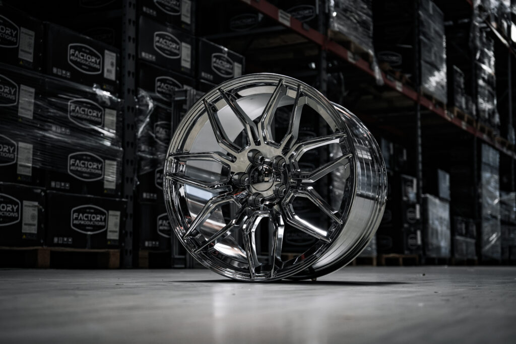 DSC06545 - Factory Reproductions FR401F replica wheel for corvettes in chrome in a warehouse setting on a concrete floor.
